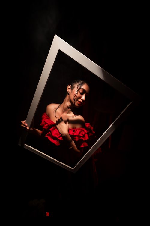 Free Stylized shot of a woman in a red dress and spotlight, holding a picture frame. Stock Photo