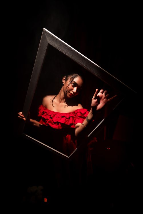Free A creative, dramatic portrait of a woman in a red dress holding a frame, set against a dark background. Stock Photo