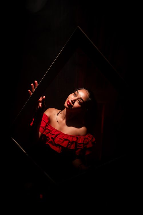 Free Elegant and moody portrait of a woman posing inside a frame with dramatic lighting. Stock Photo