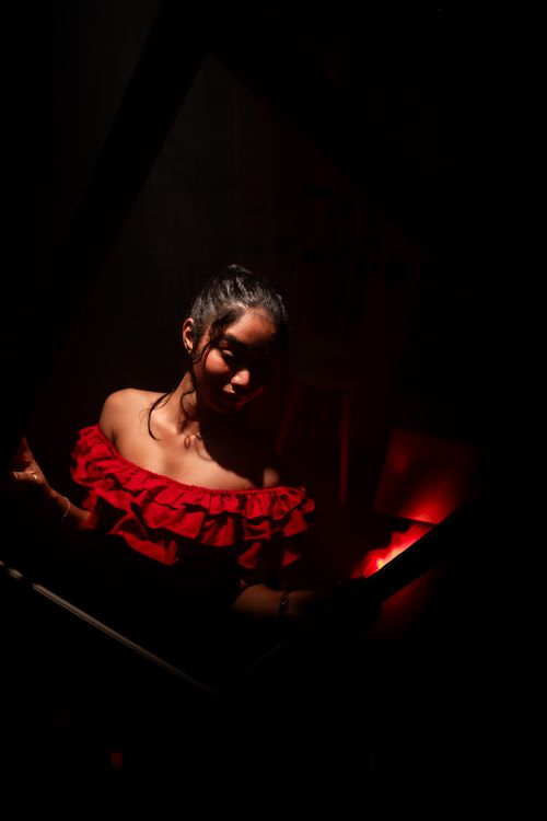 Free A striking portrait of a woman in a red dress, captured in intense lighting. Perfect for creative projects. Stock Photo