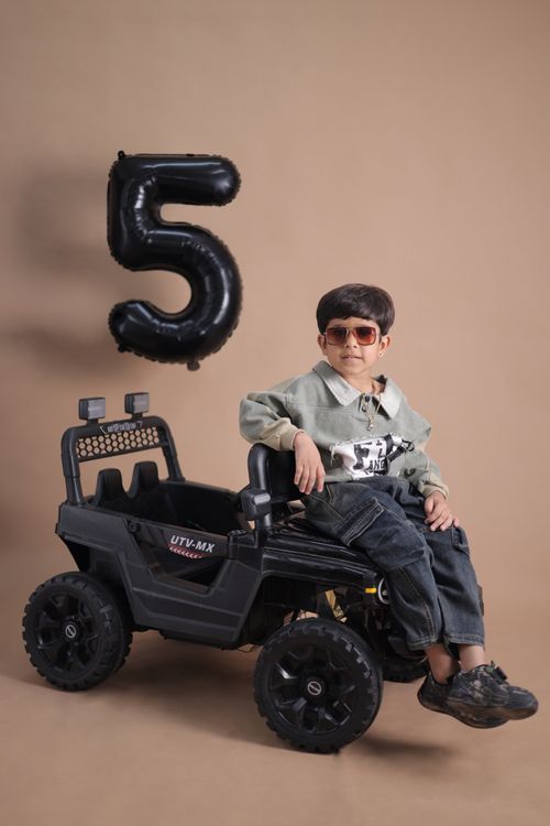 Free Child celebrating fifth birthday with a black balloon and ride-on toy car. Stock Photo