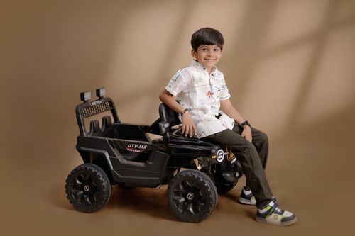 Free Young boy in a white shirt joyfully rides a black toy car indoors. Stock Photo