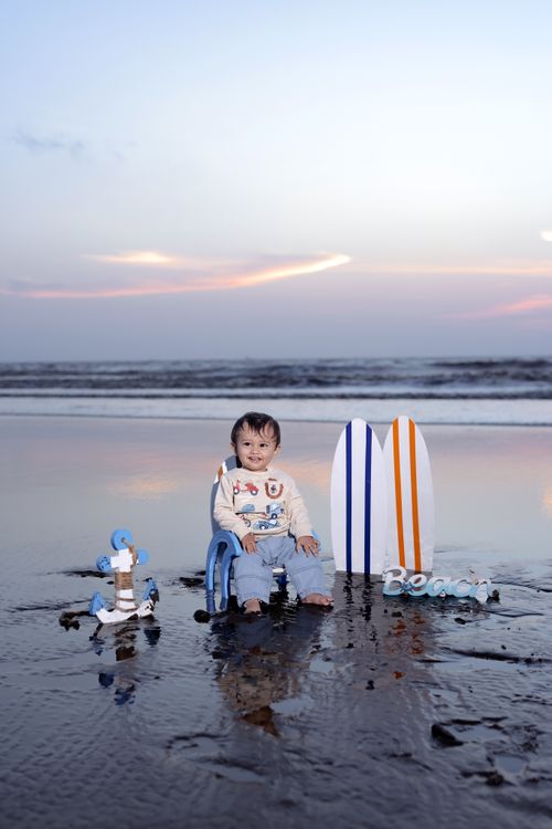 Free A smiling child plays with toy surfboards by the beach at sunset, creating a joyful seaside scene. Stock Photo