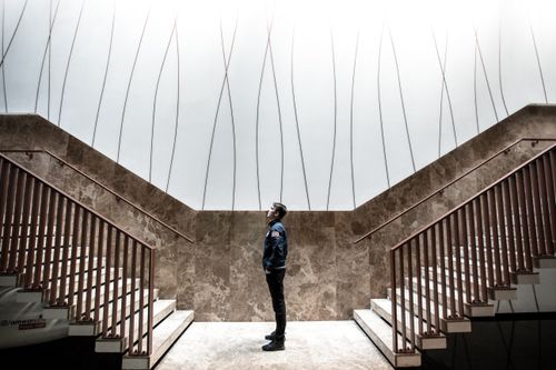 Free A person stands indoors, observing the modern architecture of symmetrical staircases with a bright ceiling above. Stock Photo