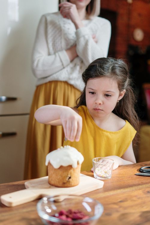 Free A young girl decorates an Easter cake with icing and sprinkles in a cozy kitchen setting. Stock Photo