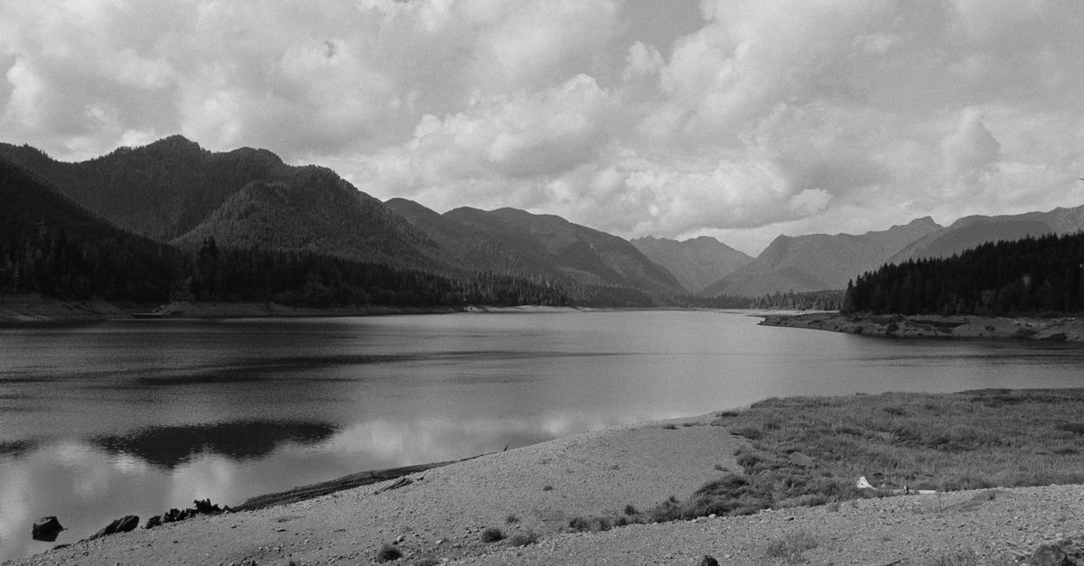 Black and white landscape view of a peaceful lake with surrounding mountains and clouds in WA, USA.