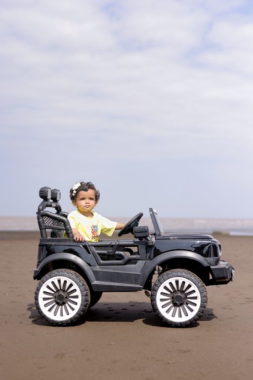 Free A toddler driving a toy car on a sandy beach under a partly cloudy sky. Stock Photo