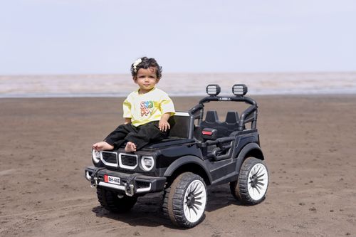 Free Cute toddler on a toy car at the beach smiling under a sunny sky. Stock Photo