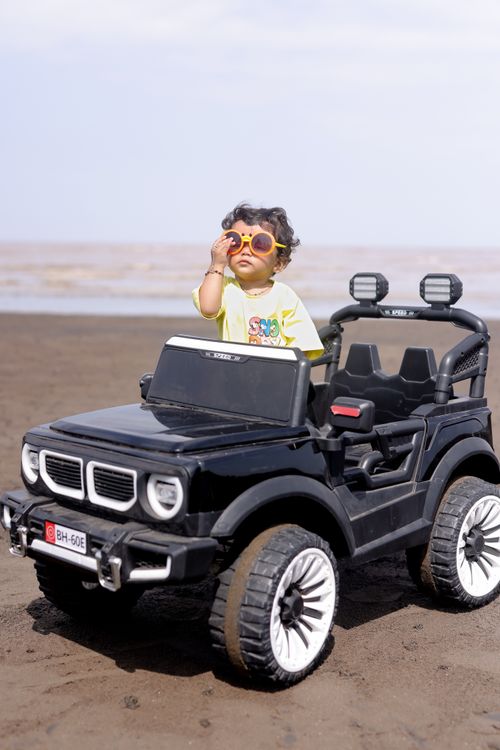 Free A child in sunglasses drives a black toy car on a sunny beach day. Stock Photo