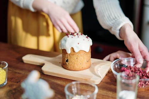 Person Holding Brown Cupcake With White Icing on Brown Wooden Table