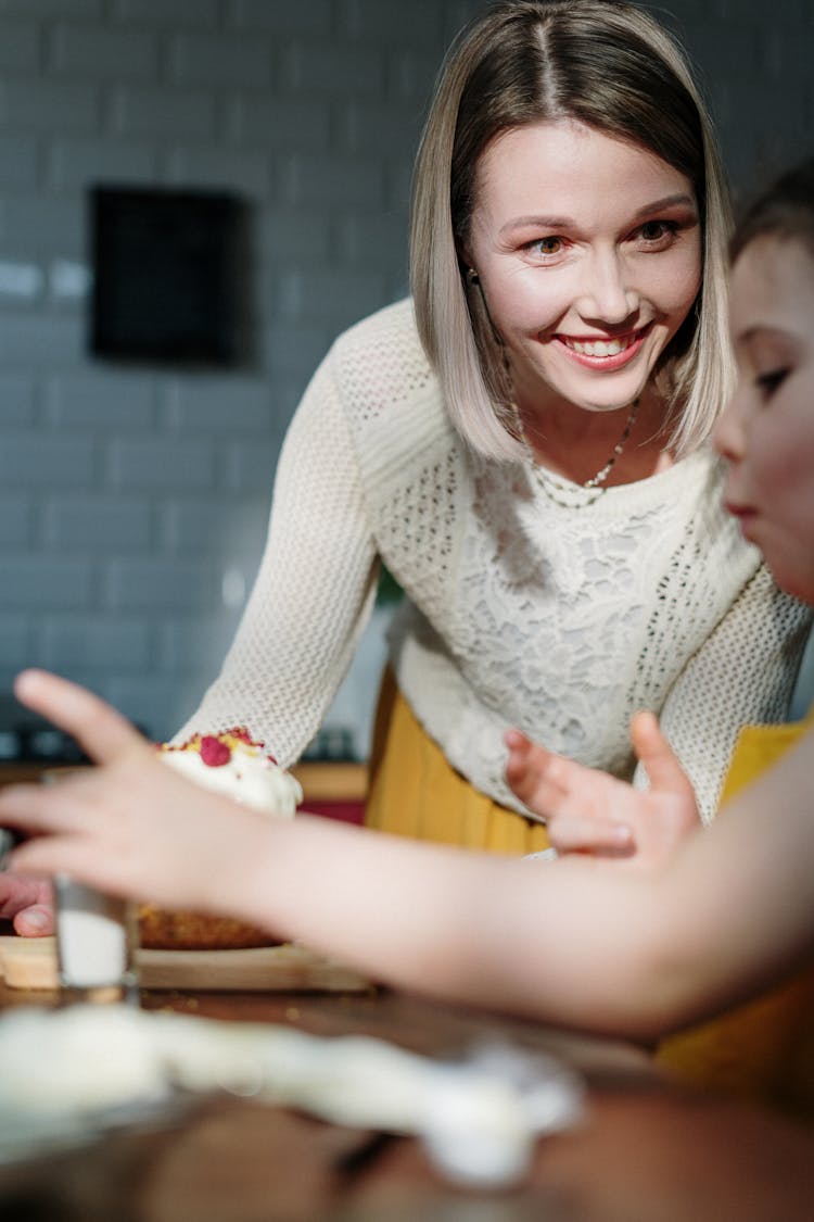 Woman In White Knit Sweater Smiling Helping In Decorating A Cake