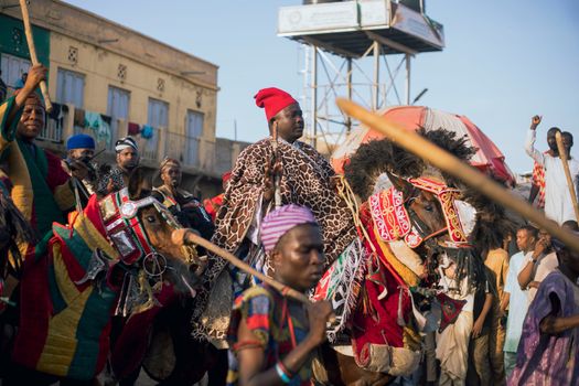 Vibrant cultural parade featuring traditional attire, horses, and an engaged audience.