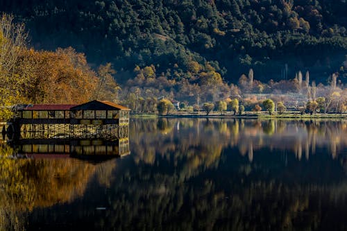 Small house on shore of lake reflecting colorful trees on autumn day