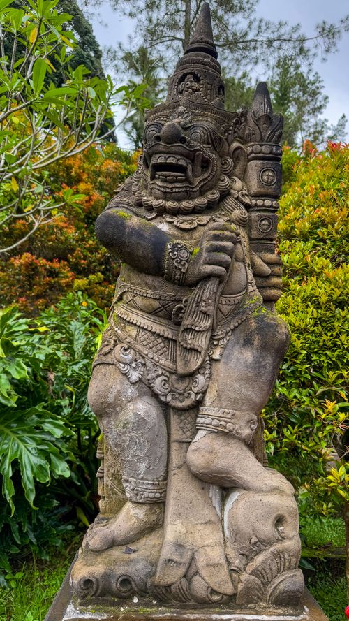 Free A detailed Balinese stone guardian statue stands amidst vibrant garden foliage, showcasing traditional craftsmanship. Stock Photo