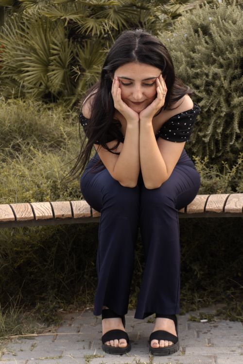Free A woman in deep thought sits on a park bench surrounded by nature. Stock Photo