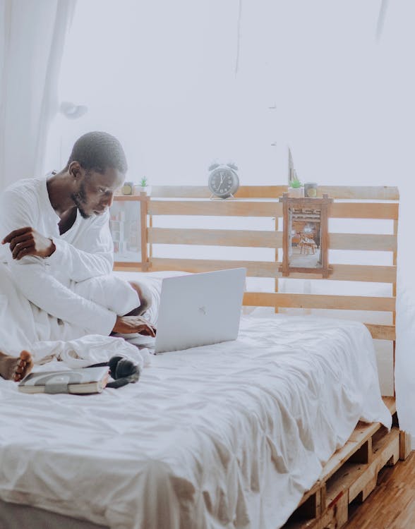 Free Man in White Thobe Sitting on Bed Using Silver Macbook Stock Photo
