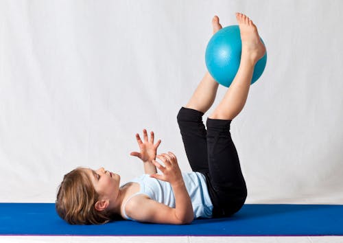 Free Girl in White Shirt and Black Pants Lying on Blue Exercise Ball Stock Photo