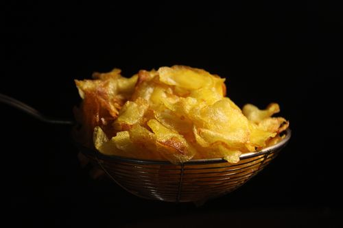 Free Close-up of homemade potato chips in a wire basket against a dark background. Stock Photo