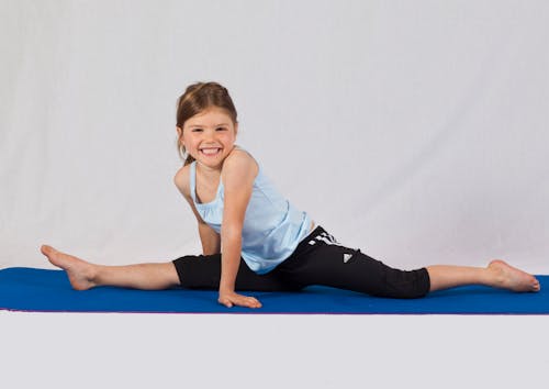 Free Girl in Blue Tank Top and Black Pants Splitting on Blue Yoga Mat Stock Photo