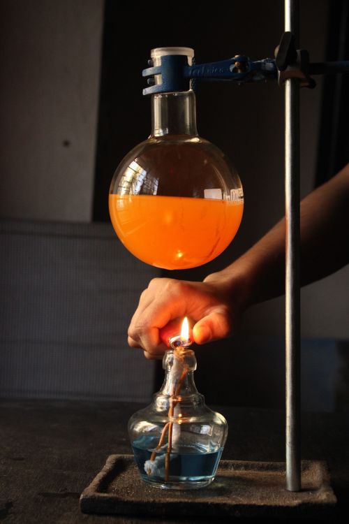 Free A scientist conducts an experiment with an orange liquid in a flask over a blue flame. Stock Photo