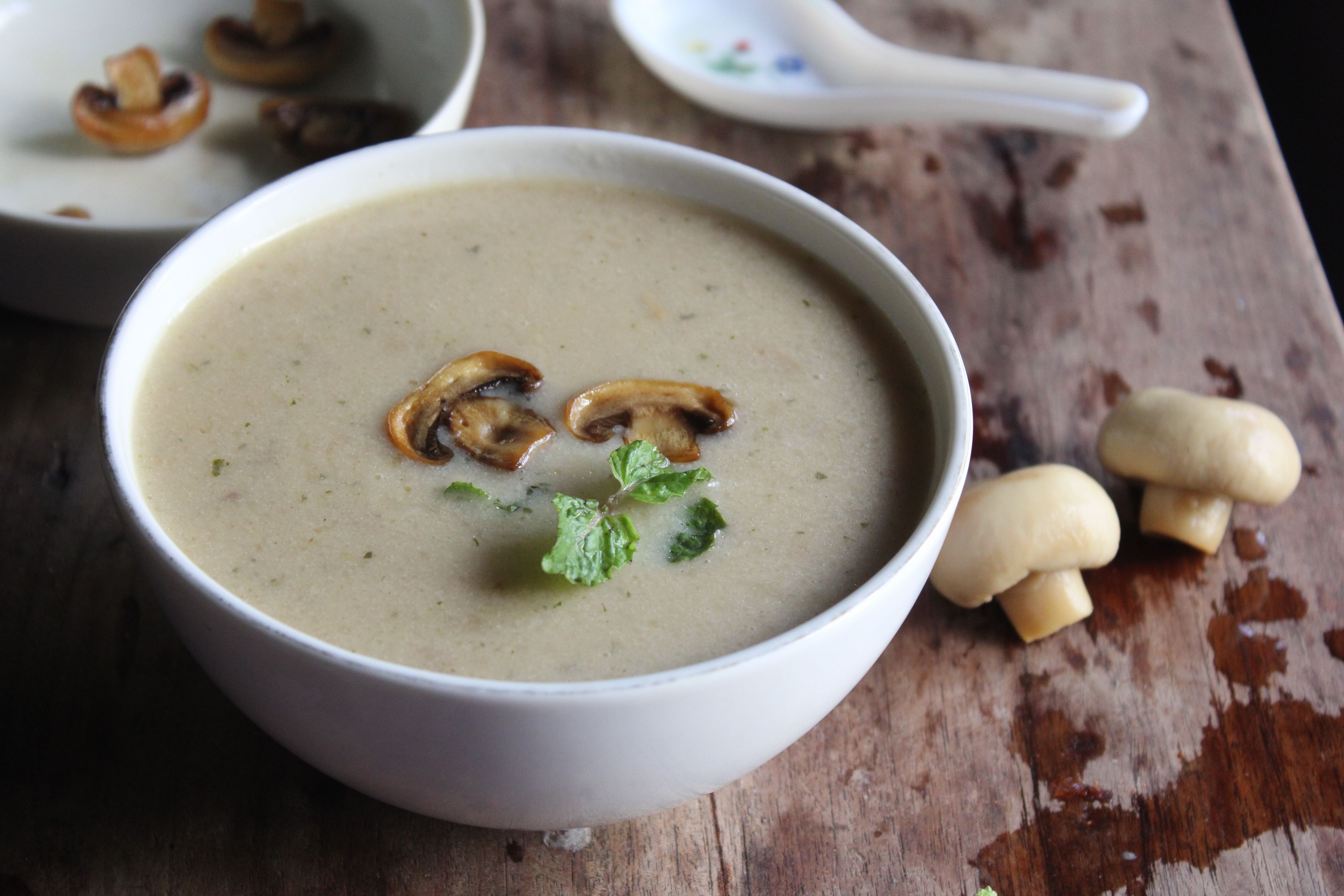 Savory mushroom soup in a white bowl with fresh herbs and sliced mushrooms on a rustic table.