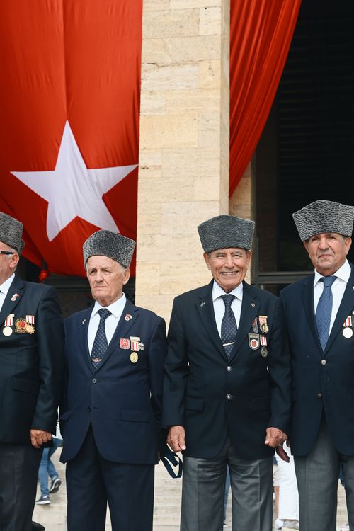 Free Turkish veterans in formal attire stand proudly before a large national flag in Ankara, Türkiye. Stock Photo