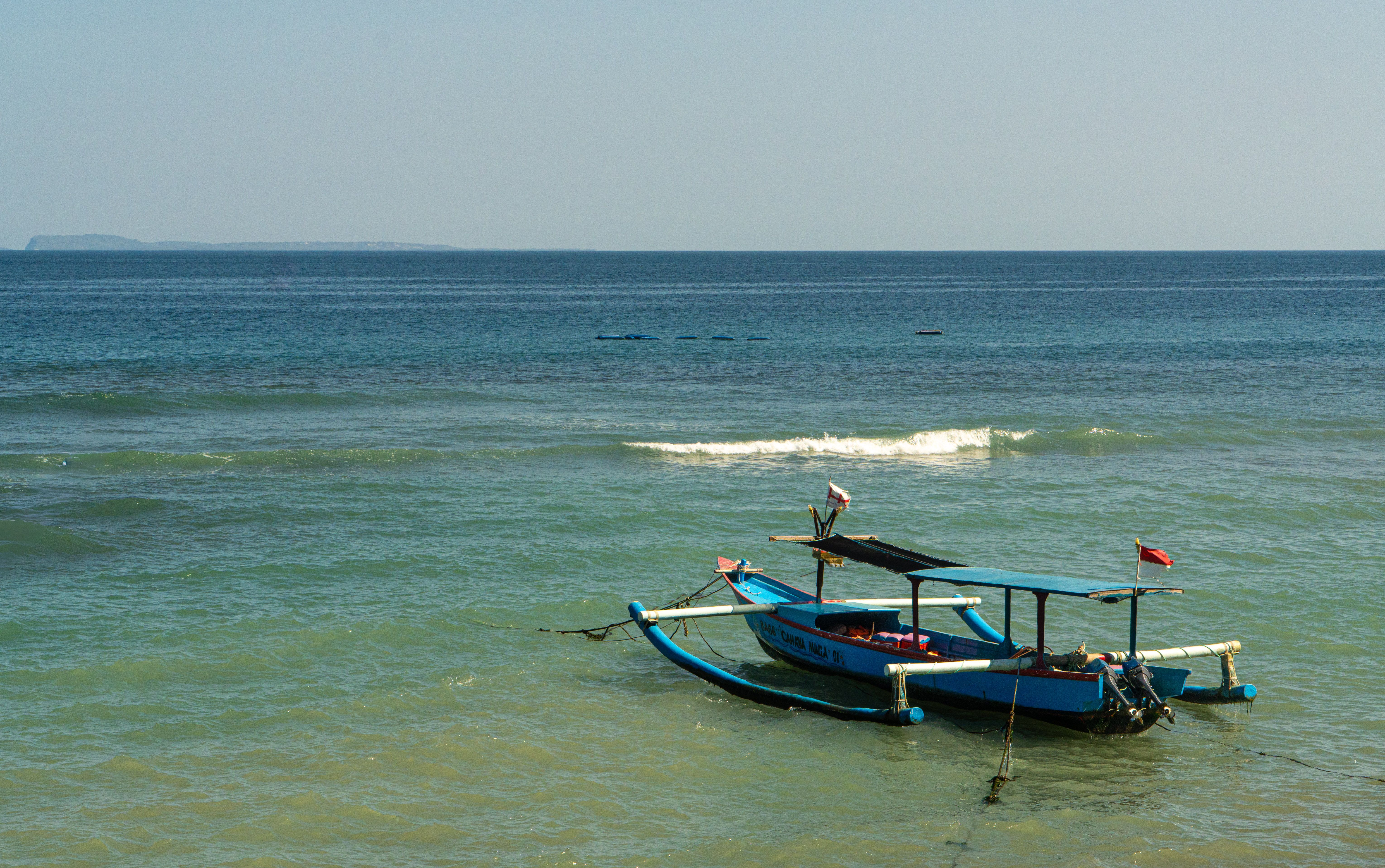 A scenic view of an outrigger canoe floating gently in the clear waters off Bali, Indonesia.