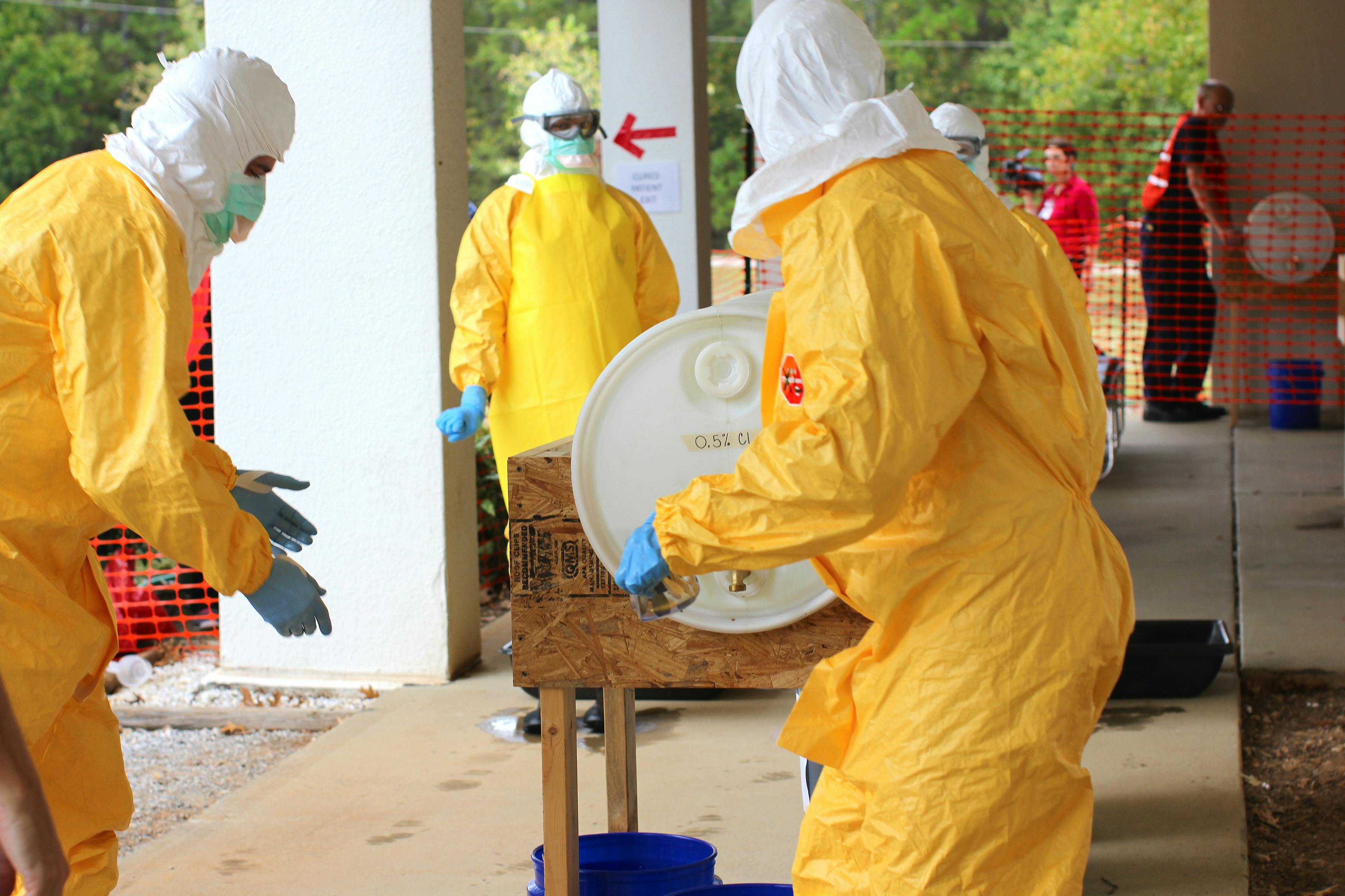 People in yellow hazmat suits working near a white container outdoors; preparing for a potential contamination.