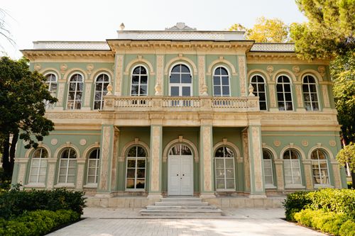 Free A stunning two-story historical building featuring classic green and cream architecture surrounded by lush trees. Stock Photo