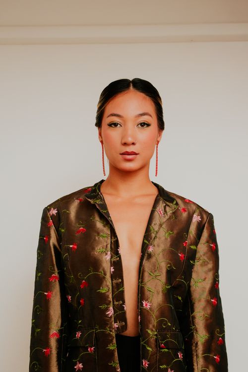 Free A fashionable woman wearing an embroidered jacket against a neutral backdrop. Stock Photo