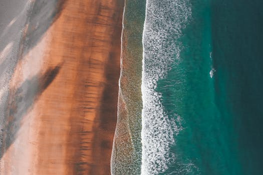 Stunning aerial view of turquoise waves meeting sandy shoreline, creating a vibrant coastal scene.