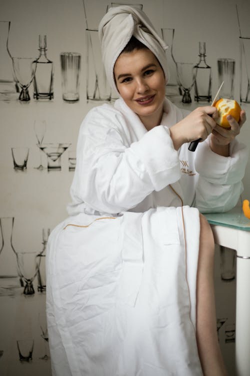 Woman in White Robe Holding Orange Fruit