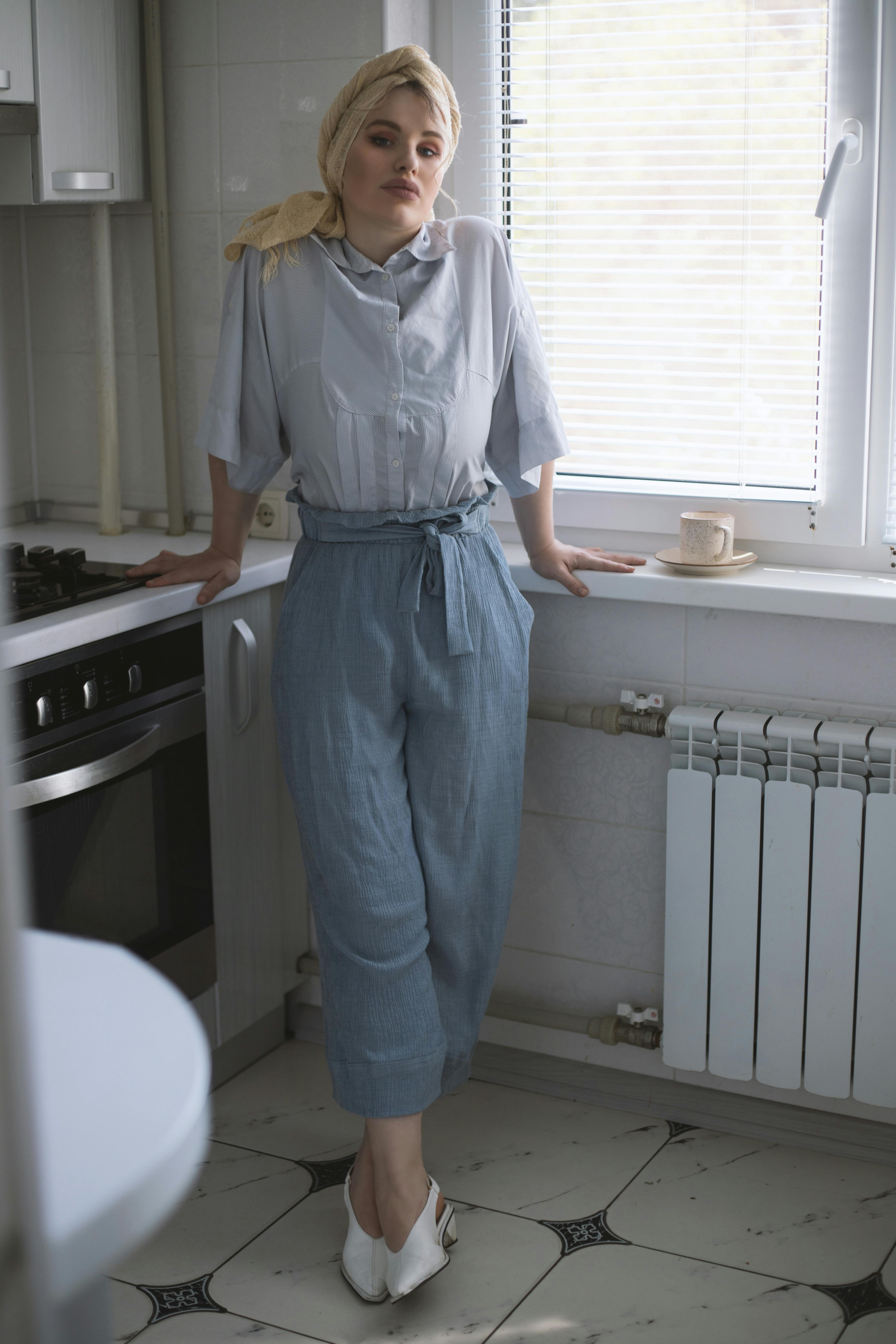 A fashionable woman in casual attire poses in a modern kitchen with natural light.