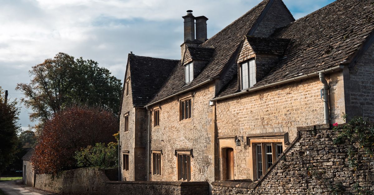 Picturesque Cotswold stone house with autumn trees, classic English countryside architecture.