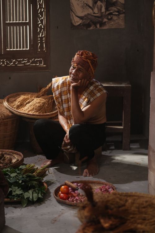 Free Elderly man in traditional attire surrounded by herbs and vegetables, deep in thought. Stock Photo