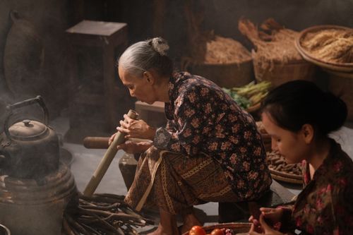 Free An elderly woman using traditional tools to cook indoors, symbolizing heritage and cultural practices. Stock Photo