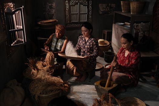 Women engage in traditional rice processing, showcasing cultural heritage in an Asian village setting.