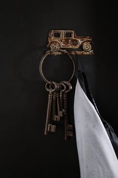 Close-up of vintage metal keys hanging on an antique car-themed hook against a dark background.