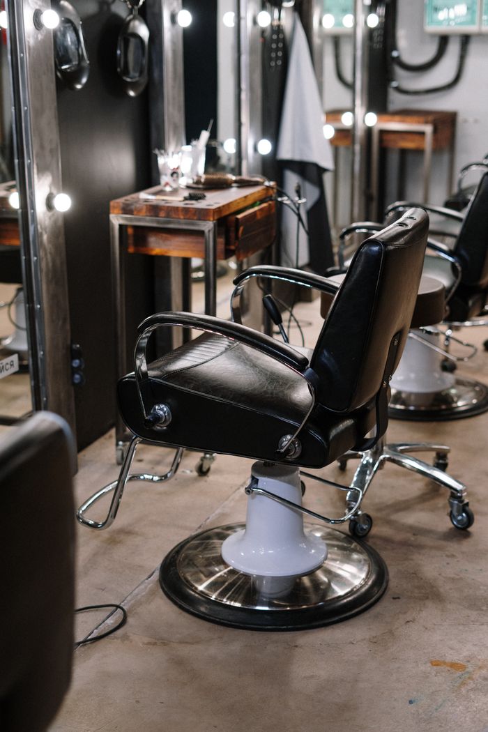 Empty black leather barber chair in front of a row of lit mirrors