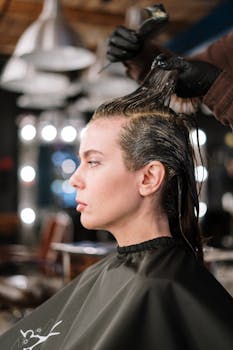 Professional hair stylist applying dye to woman's hair in a salon setting.