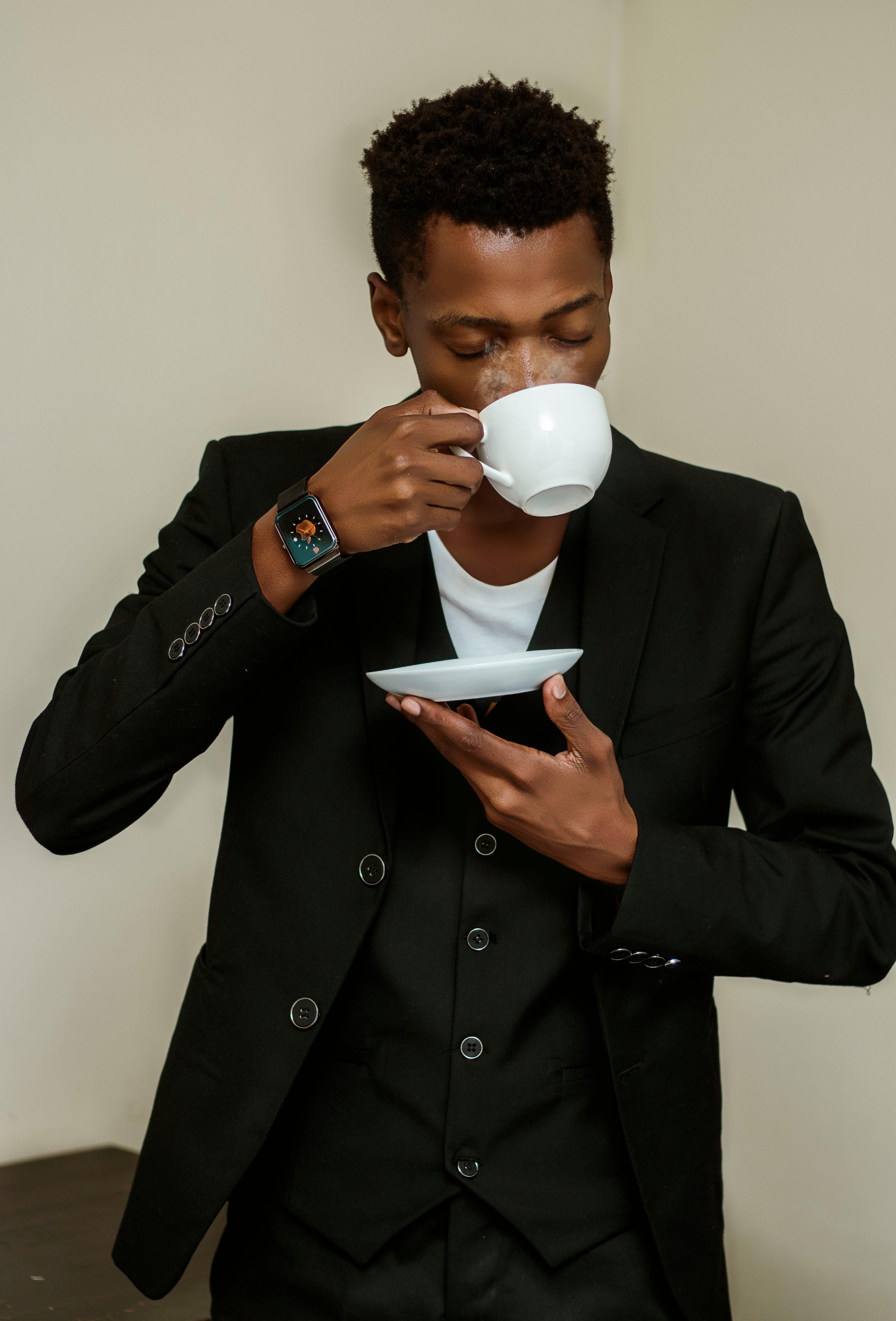 man in black suit holding white ceramic mug