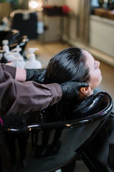 A professional hairstylist washing a woman's hair in a modern salon setting, ensuring quality haircare.
