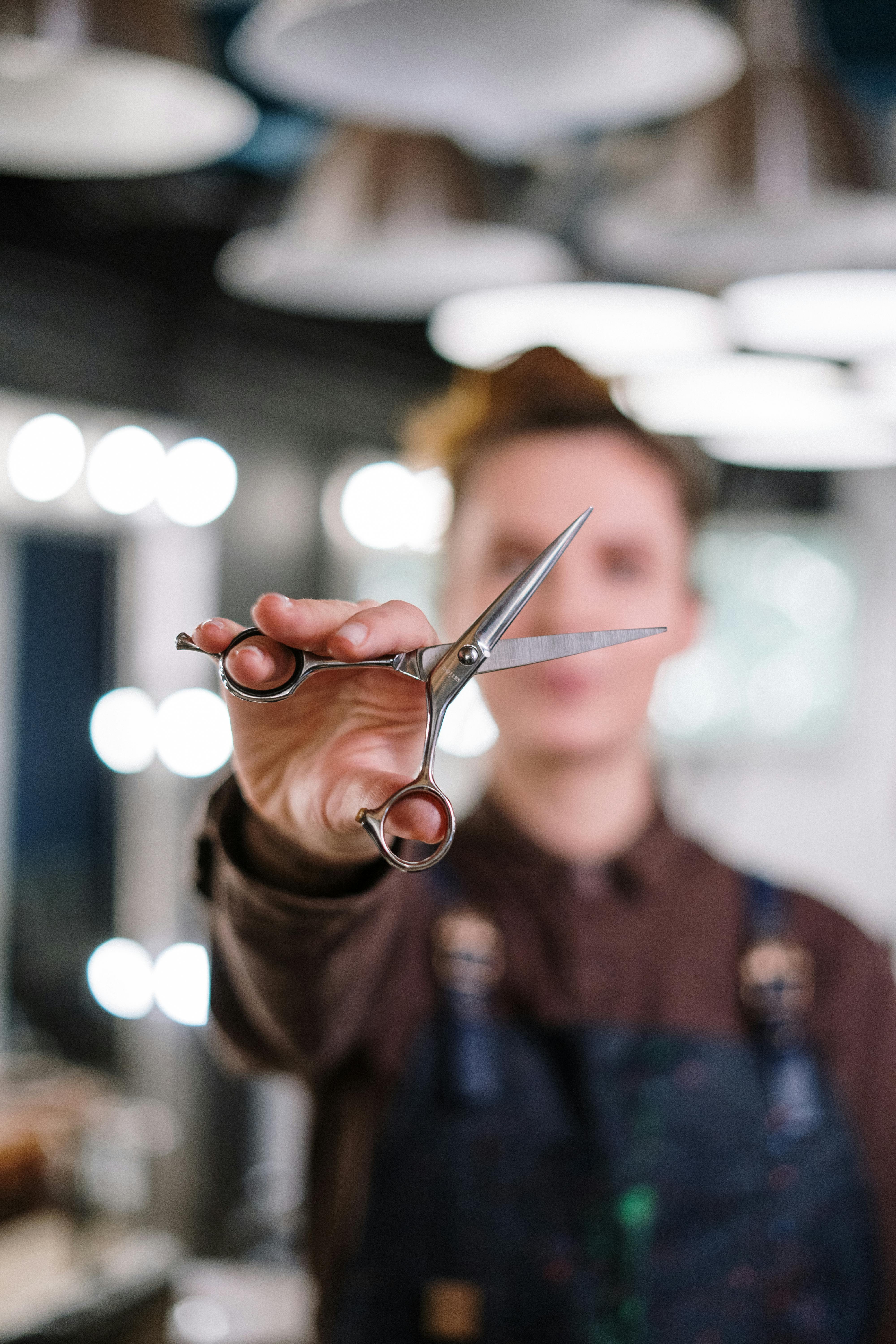 person in brown long sleeve shirt holding silver scissors