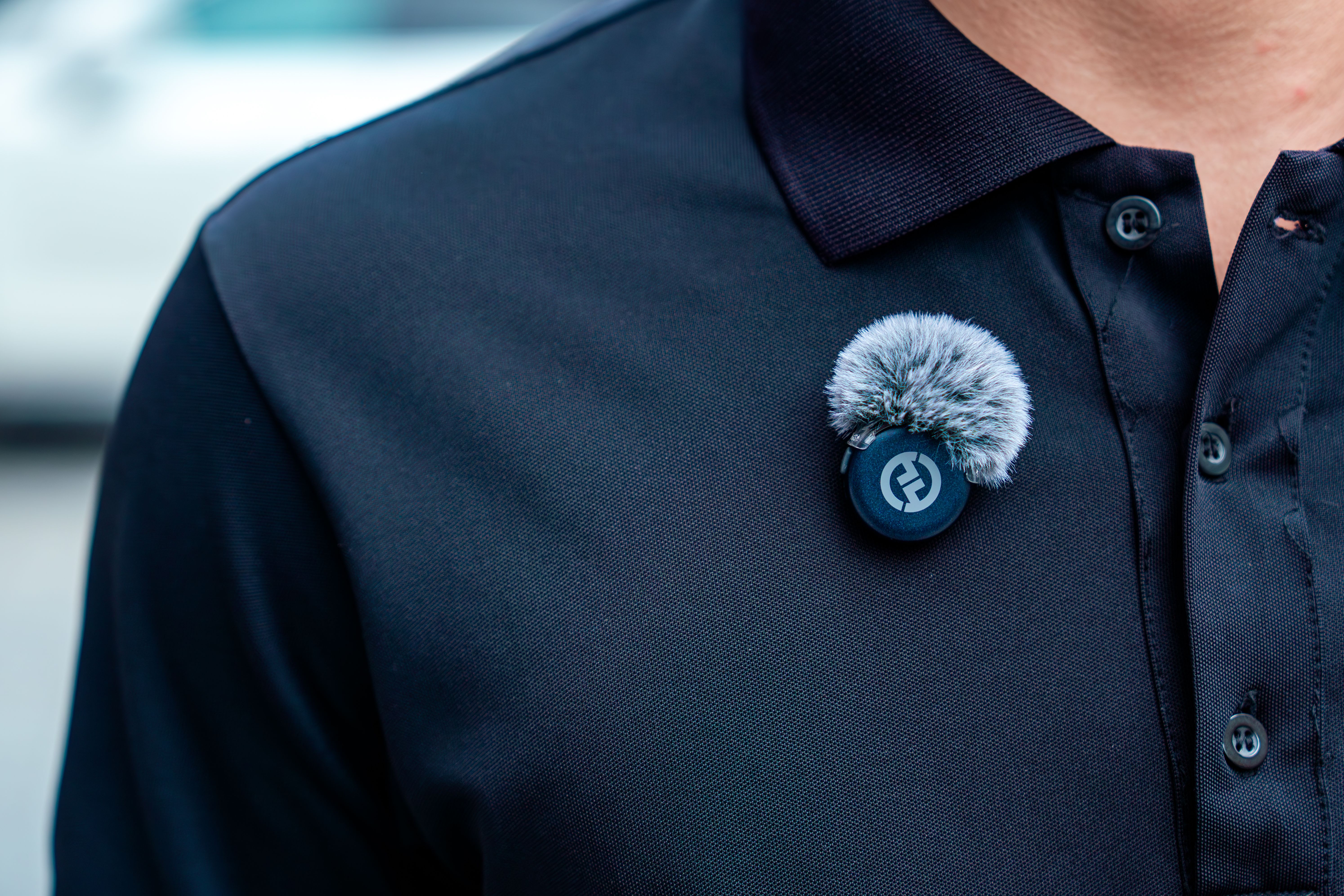 Close-up of a lavalier microphone attached to a black polo shirt, ideal for audio recording.