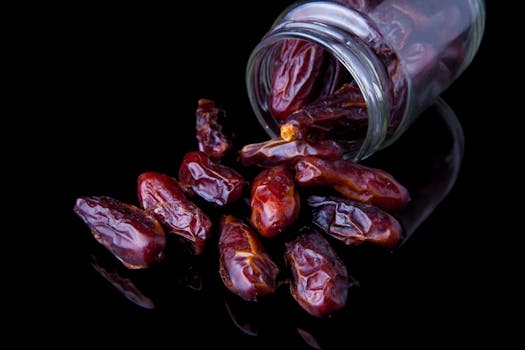 Dark and rich dried dates spilling from a glass jar on a glossy surface.