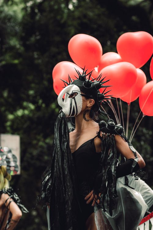 Free Striking masked figure with spikes holding red balloons at an outdoor festival. Stock Photo
