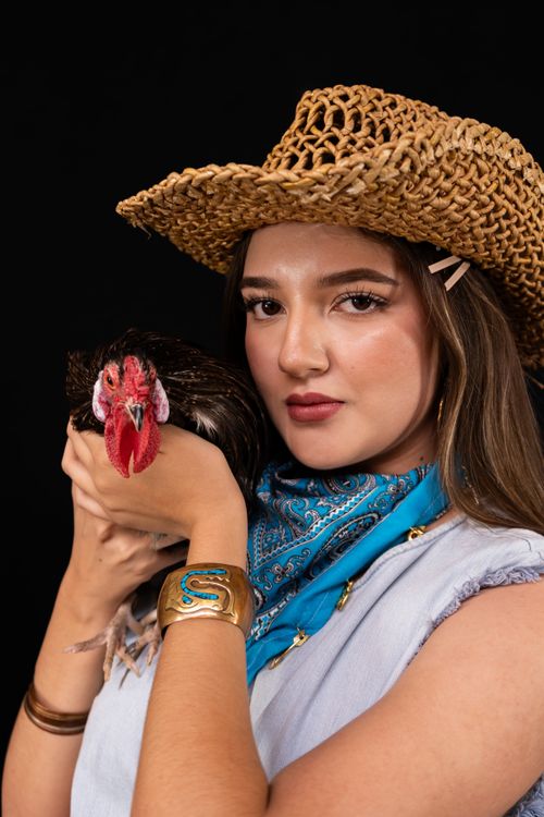 Free Portrait of a young woman wearing a cowboy hat holding a hen close up with a black backdrop. Stock Photo
