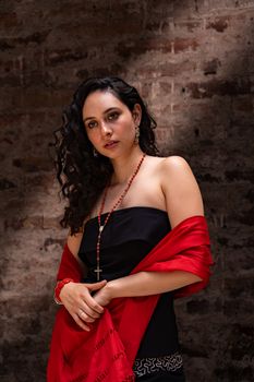 Striking portrait of a woman with a red shawl against a textured brick wall.