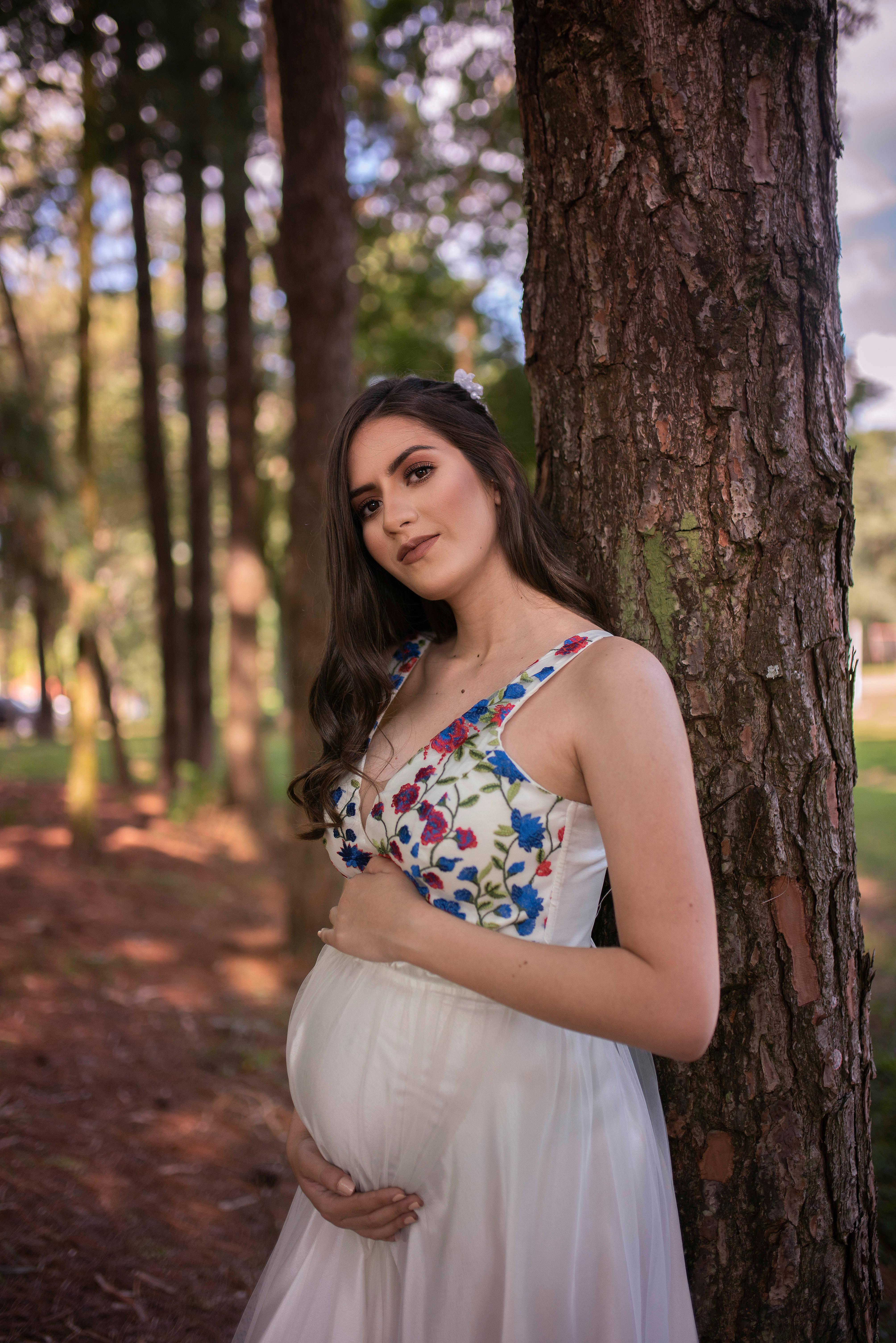 woman in white spaghetti strap dress standing beside brown tree