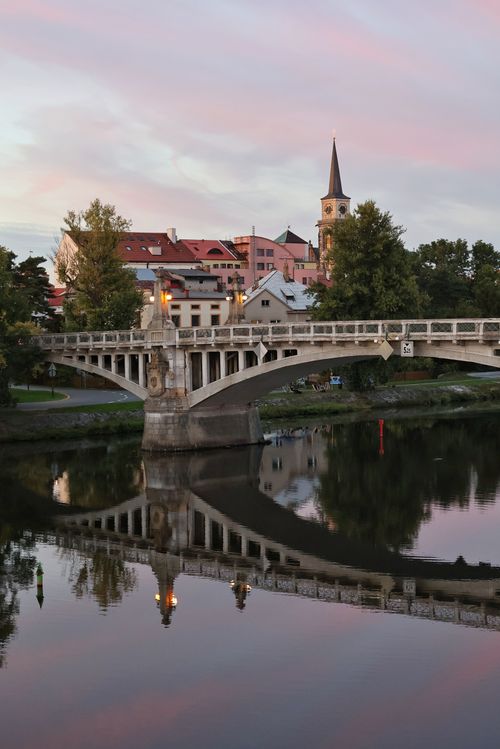 Free Beautiful scenery of a riverside bridge and town at twilight, reflecting in calm water. Stock Photo